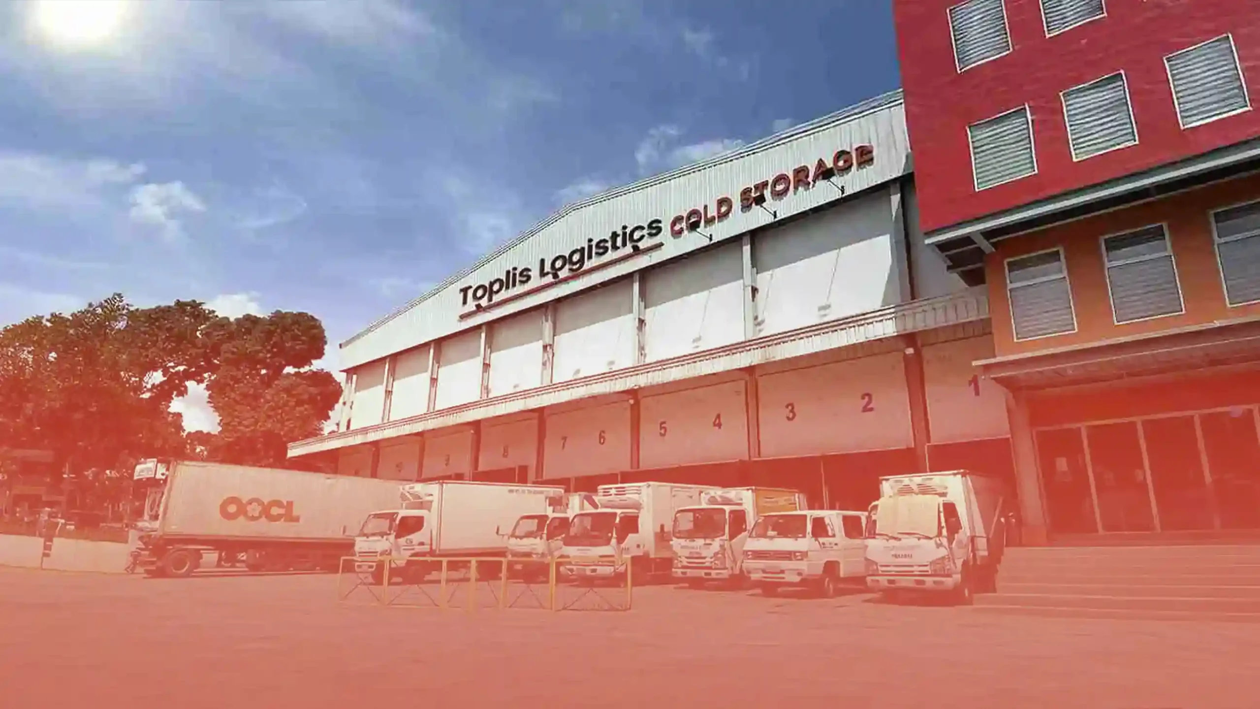 Toplis Logistics Cold Storage facility with numbered loading docks, refrigerated trucks, and an OOCL container truck under a clear sky.