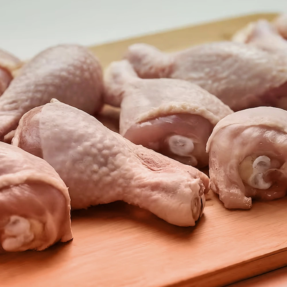 leg-cut chicken neatly piled on a brown chopping board in a symmetrical position with light background